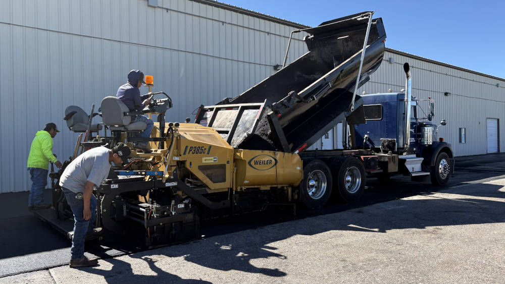 Crew with paver installing new hot mix asphalt.